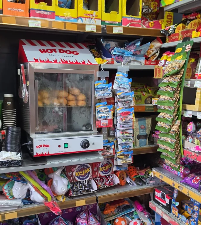 Máquina de perritos calientes con panecillos dentro, en una estantería de la tienda junto a snacks y chucherías